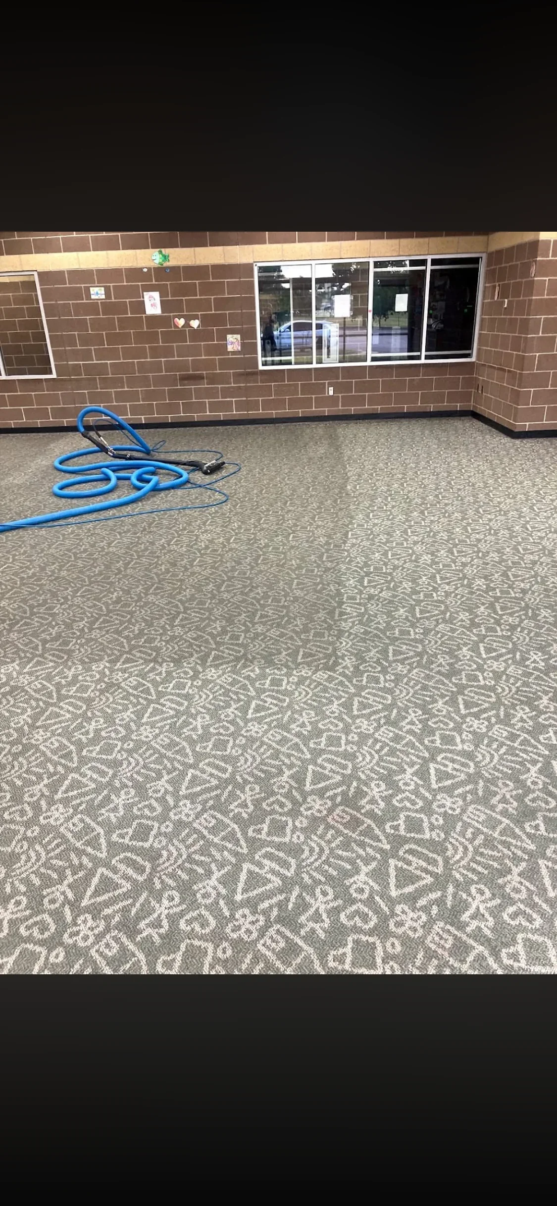 Professional carpet cleaning in progress with extraction hose on patterned commercial carpet