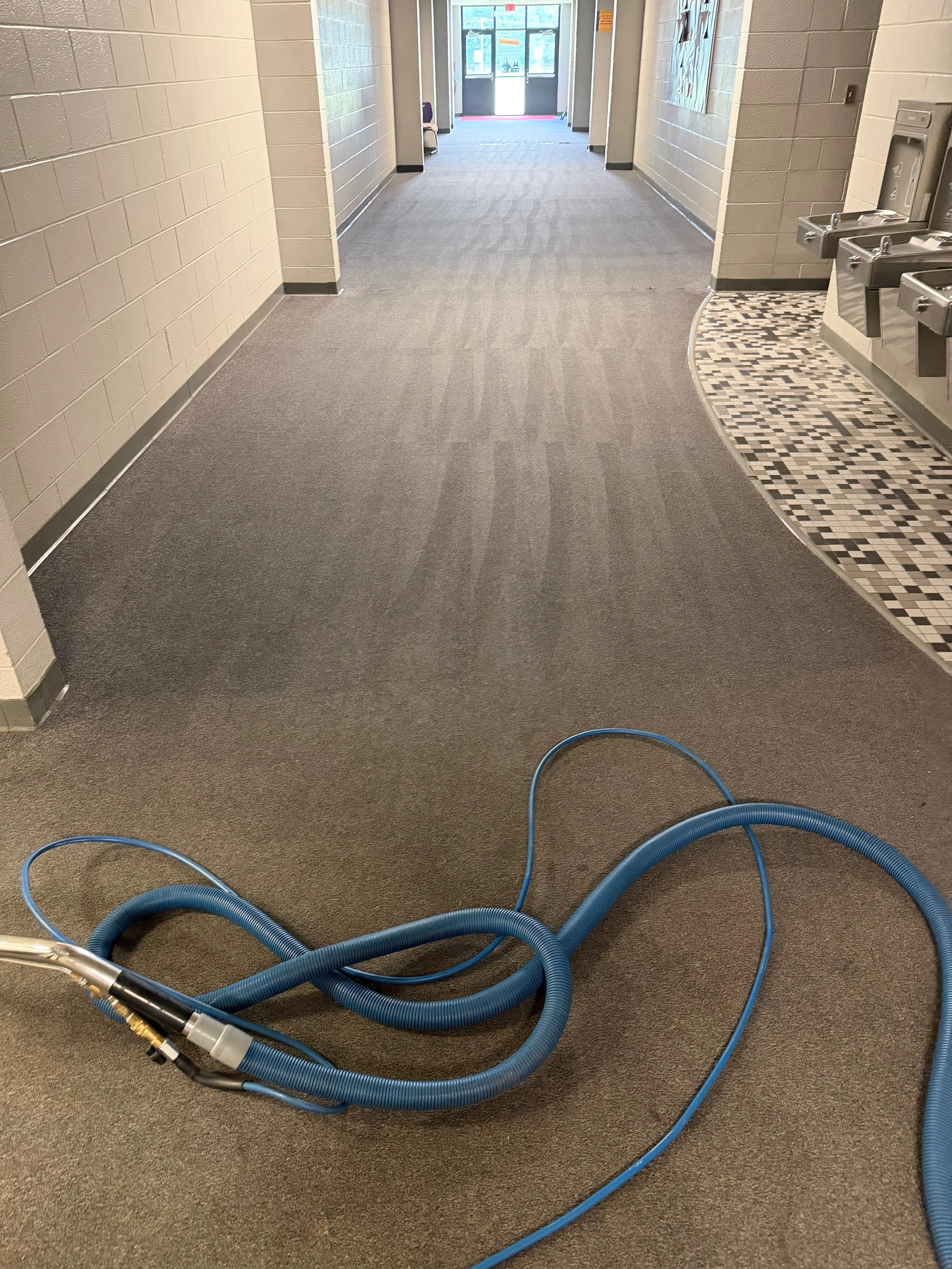 Professional carpet cleaning in progress in commercial hallway with gray carpet and tile flooring